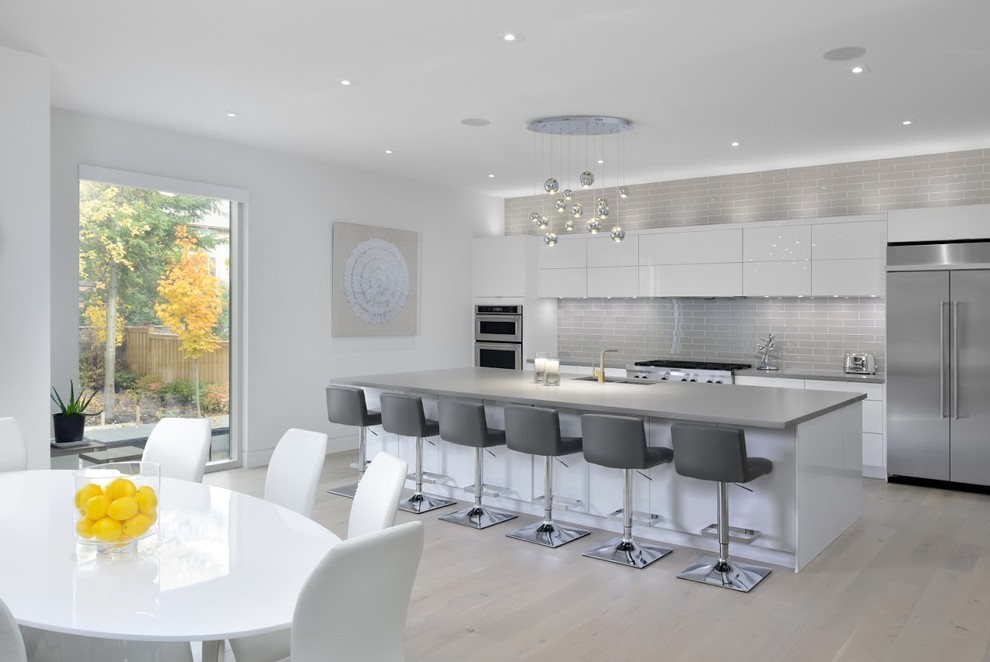 Inspiration for a mid-sized contemporary eat-in kitchen in Toronto with a double-bowl sink, flat-panel cabinets, white cabinets, grey splashback, subway tile splashback, stainless steel appliances, with island, beige floor and light hardwood floors.