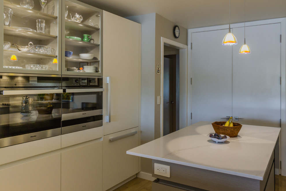 Inspiration for a mid-sized modern u-shaped light wood floor eat-in kitchen remodel in New York with an undermount sink, flat-panel cabinets, beige cabinets, solid surface countertops, green backsplash, glass tile backsplash, stainless steel appliances and an island
