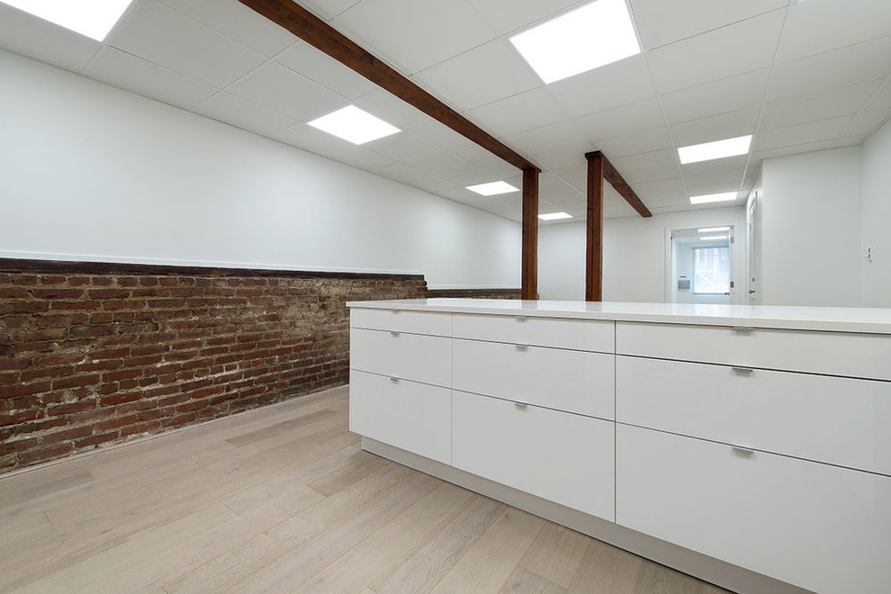 This is an example of a mid-sized industrial u-shaped open plan kitchen in San Francisco with an undermount sink, flat-panel cabinets, white cabinets, solid surface benchtops, stainless steel appliances, light hardwood floors, a peninsula and beige floor.