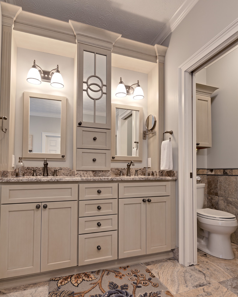 Inspiration for a large traditional master bathroom in Atlanta with raised-panel cabinets, beige cabinets, a two-piece toilet, gray tile, travertine, porcelain floors, an undermount sink, granite benchtops, a drop-in tub, beige walls, beige floor, beige benchtops and a double vanity.