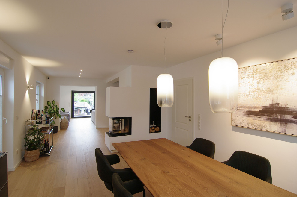 Geräumige Moderne Wohnküche mit weißer Wandfarbe, braunem Holzboden, Kaminofen, verputzter Kaminumrandung, beigem Boden und Tapetenwänden in Düsseldorf