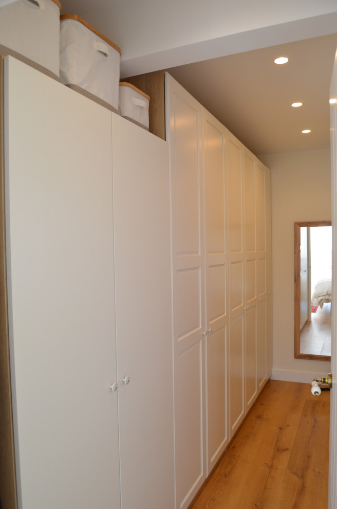 Foto de armario vestidor unisex escandinavo pequeño con armarios con rebordes decorativos, puertas de armario blancas y suelo de madera clara