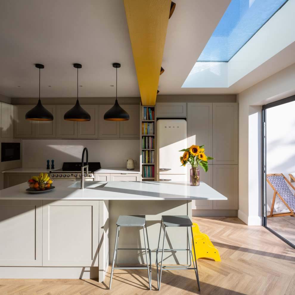 Design ideas for a mid-sized modern single-wall eat-in kitchen in Essex with a double-bowl sink, recessed-panel cabinets, grey cabinets, quartzite benchtops, white splashback, timber splashback, coloured appliances, vinyl floors, with island, brown floor, white benchtop and exposed beam.