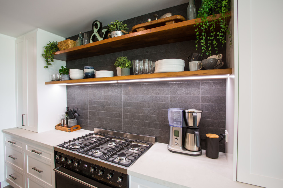 This is an example of an expansive country galley eat-in kitchen in Brisbane with a double-bowl sink, recessed-panel cabinets, black cabinets, wood benchtops, black splashback, subway tile splashback, black appliances, with island, grey floor and white benchtop.