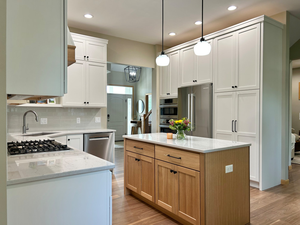Open concept kitchen - mid-sized transitional l-shaped medium tone wood floor and brown floor open concept kitchen idea with an undermount sink, flat-panel cabinets, white cabinets, quartz countertops, gray backsplash, ceramic backsplash, stainless steel appliances, an island and white countertops