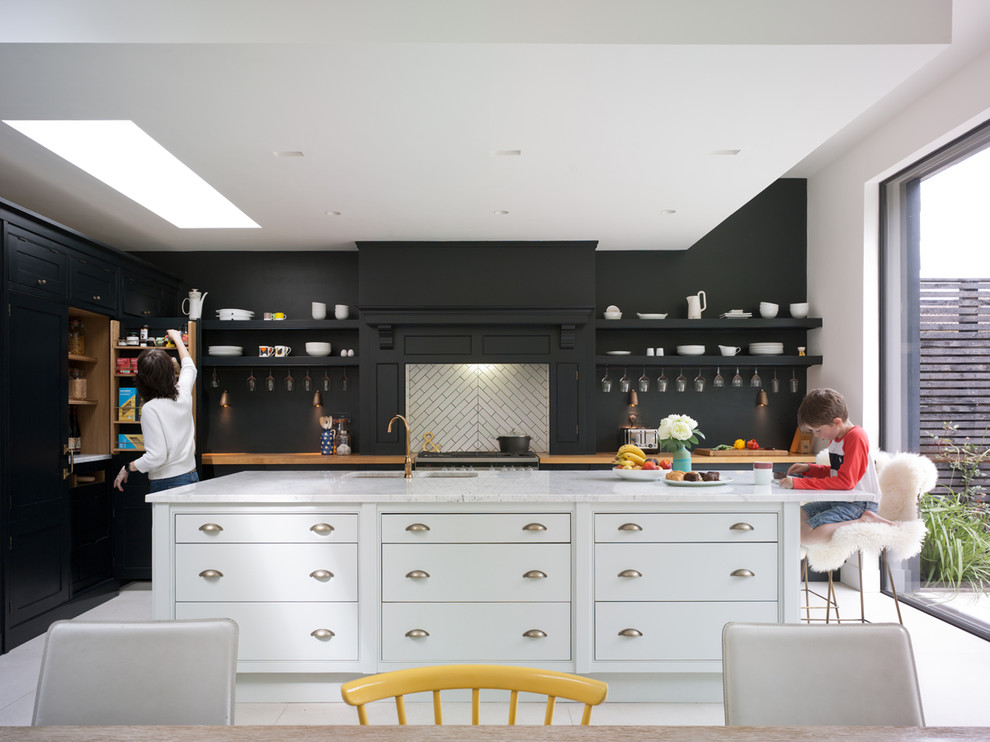 Traditional l-shaped open plan kitchen in Kent with a drop-in sink, flat-panel cabinets, black cabinets, marble benchtops, white splashback, cement tile splashback, panelled appliances, ceramic floors and a peninsula.