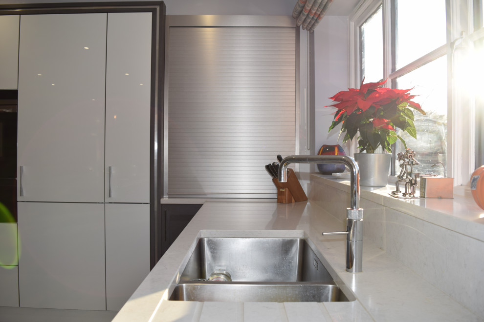 Mittelgroße Moderne Wohnküche mit integriertem Waschbecken, Schrankfronten mit vertiefter Füllung, Quarzit-Arbeitsplatte, Elektrogeräten mit Frontblende, Keramikboden, Kücheninsel, weißem Boden und weißer Arbeitsplatte in Hampshire