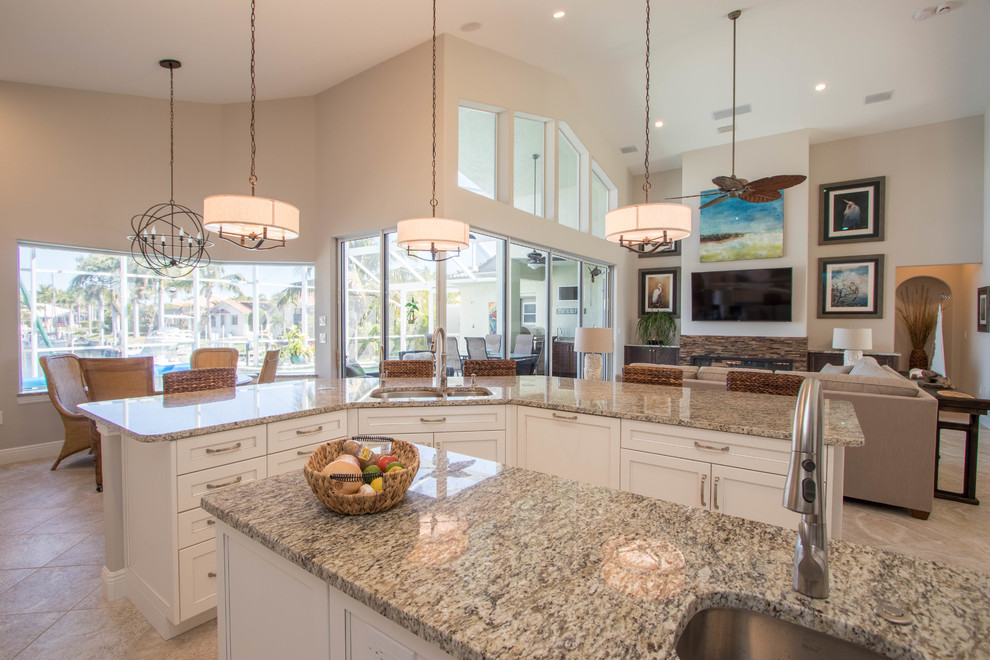 This is an example of an expansive transitional l-shaped open plan kitchen in Miami with a double-bowl sink, shaker cabinets, white cabinets, granite benchtops, beige splashback, stone tile splashback, stainless steel appliances, travertine floors and multiple islands.
