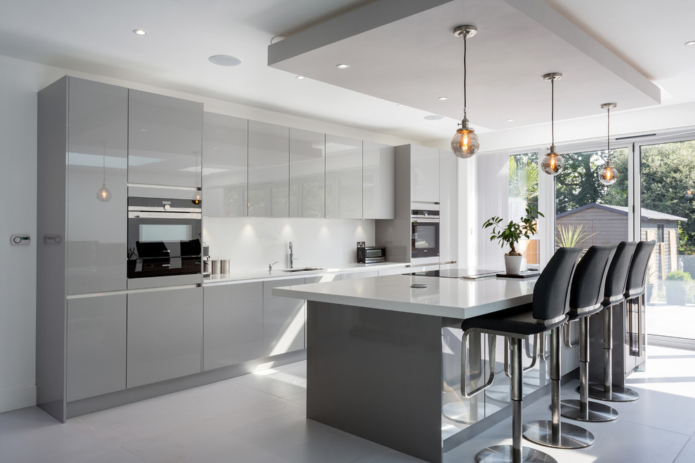 Mid-sized contemporary galley kitchen in London with an undermount sink, flat-panel cabinets, grey cabinets, stainless steel appliances, with island, white floor, white benchtop and white splashback.
