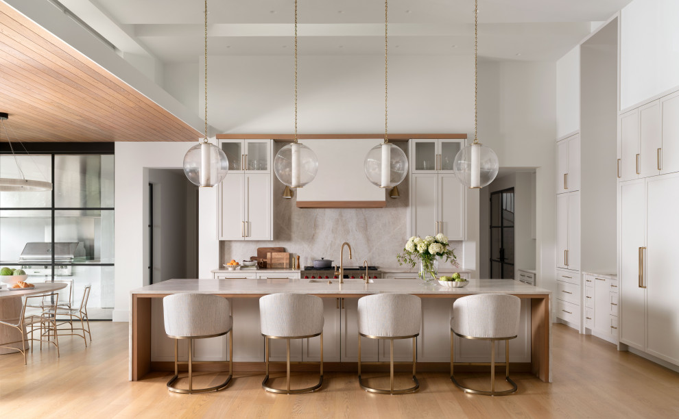 Transitional l-shaped medium tone wood floor and brown floor kitchen photo in Austin with quartzite countertops, stone slab backsplash, an undermount sink, recessed-panel cabinets, gray cabinets, gray backsplash, stainless steel appliances, an island and gray countertops
