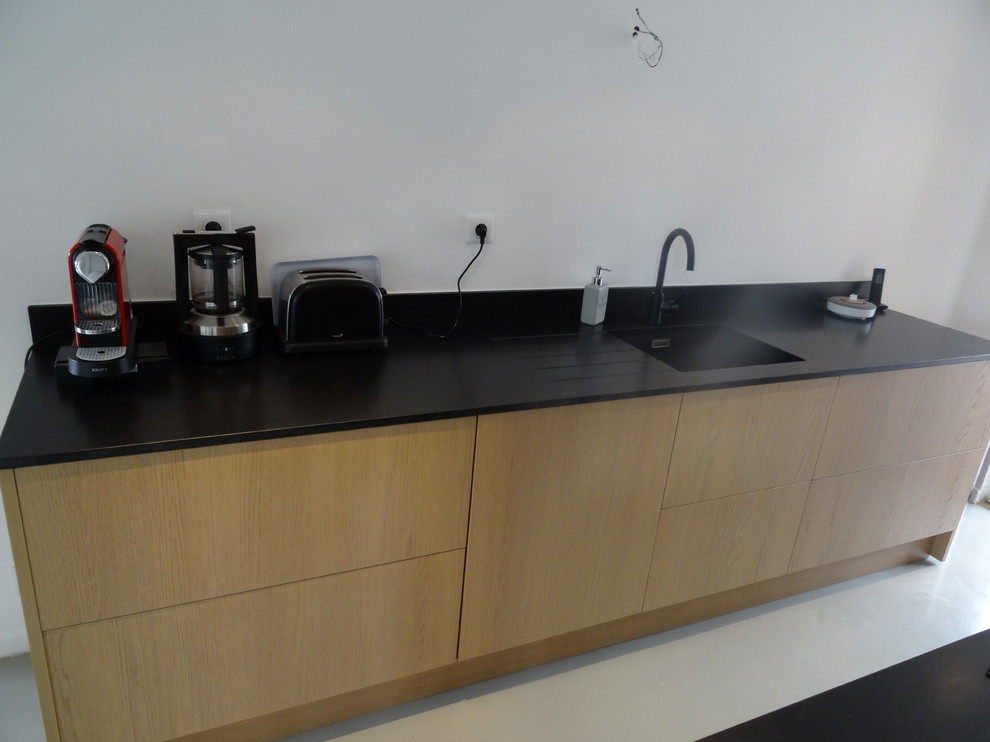 This is an example of a large industrial galley eat-in kitchen in Marseille with an integrated sink, beaded inset cabinets, black cabinets, granite benchtops, black splashback, concrete floors, with island and grey floor.