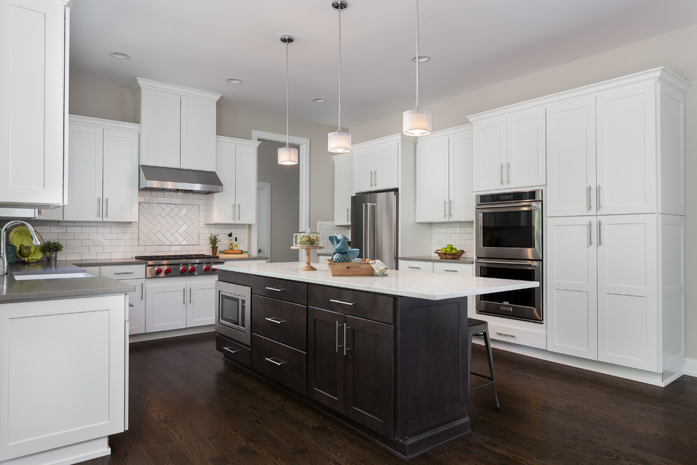 Mid-sized transitional u-shaped dark wood floor and brown floor open concept kitchen photo in Chicago with shaker cabinets, white cabinets, white backsplash, subway tile backsplash, stainless steel appliances, an island, gray countertops, a farmhouse sink and quartz countertops