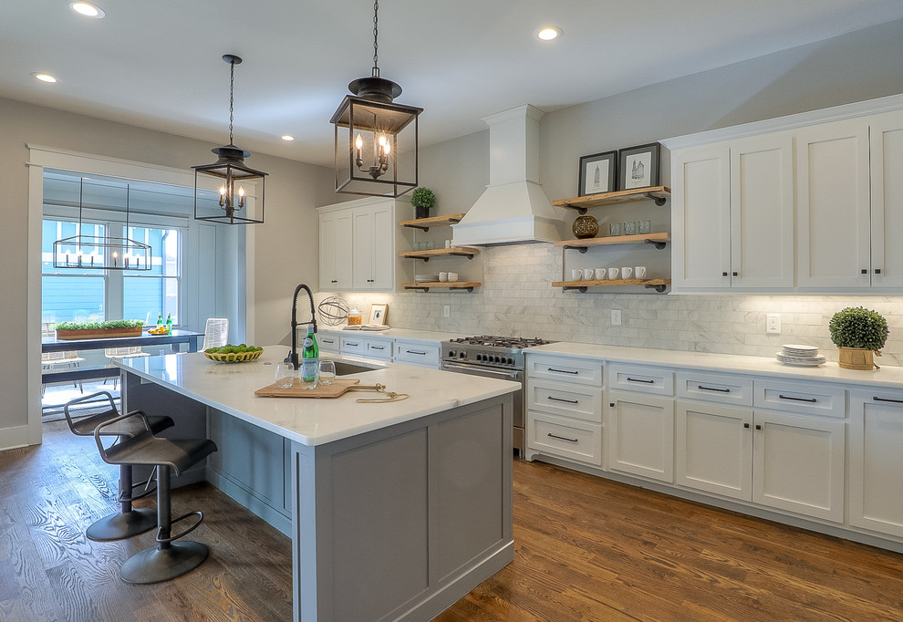 Photo of a mid-sized arts and crafts single-wall open plan kitchen in Nashville with an undermount sink, recessed-panel cabinets, white cabinets, granite benchtops, white splashback, ceramic splashback, stainless steel appliances, medium hardwood floors, with island, brown floor and white benchtop.