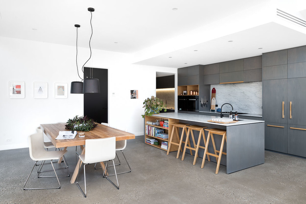 Mid-sized contemporary galley open plan kitchen in Melbourne with flat-panel cabinets, marble benchtops, marble splashback, black appliances, concrete floors, with island, grey floor, grey cabinets, white splashback and white benchtop.