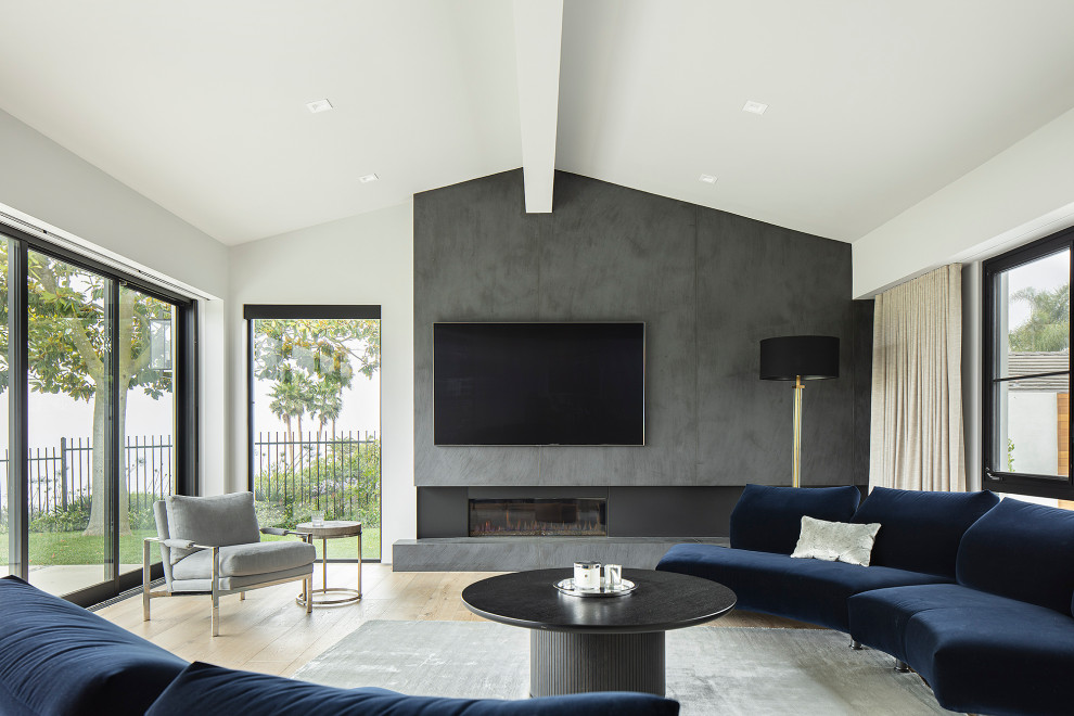 Inspiration for a large contemporary games room in Los Angeles with grey walls, light hardwood flooring, a ribbon fireplace, a metal fireplace surround, a wall mounted tv, beige floors and a vaulted ceiling.
