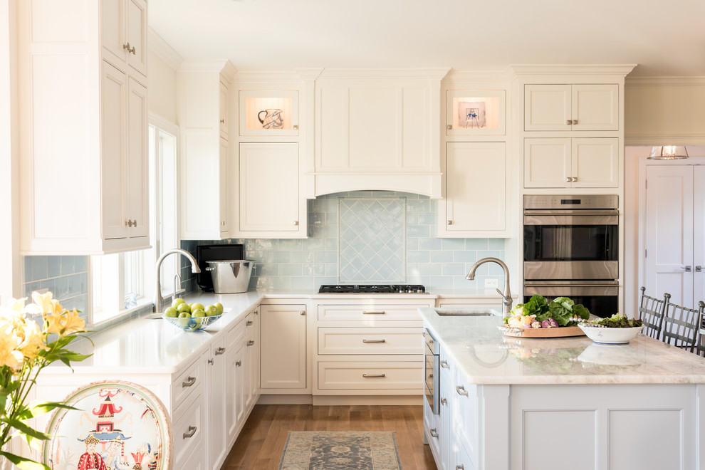 Beach style l-shaped eat-in kitchen in Boston with an undermount sink, recessed-panel cabinets, white cabinets, blue splashback, panelled appliances, light hardwood floors and with island.