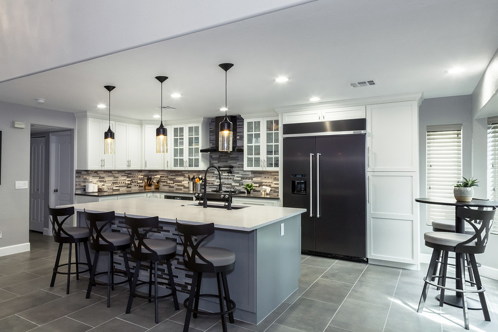 Mid-sized transitional l-shaped porcelain tile and gray floor open concept kitchen photo in Phoenix with an undermount sink, shaker cabinets, white cabinets, quartz countertops, gray backsplash, glass tile backsplash, black appliances, an island and gray countertops