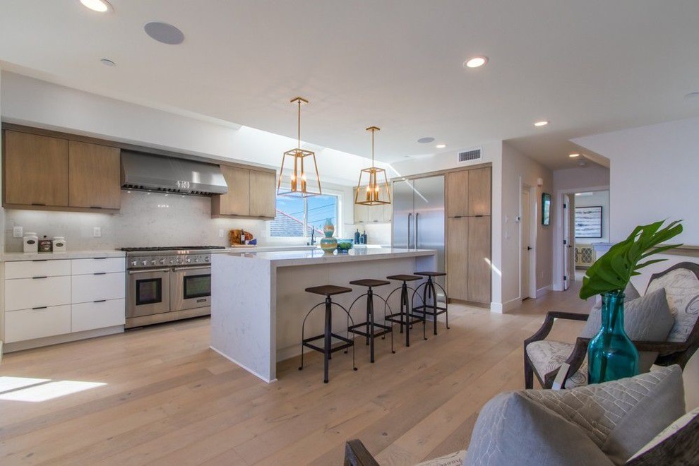 Photo of a mid-sized beach style l-shaped open plan kitchen in San Diego with flat-panel cabinets, medium wood cabinets, marble benchtops, light hardwood floors, with island and white benchtop.