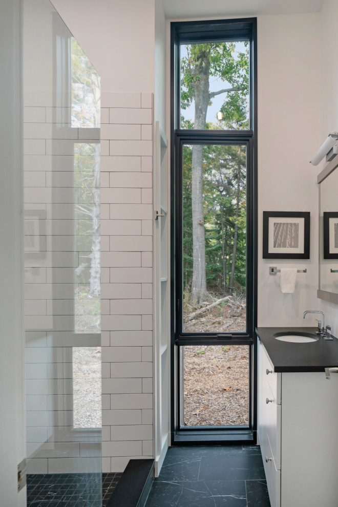 Inspiration for a mid-sized country master bathroom in Portland Maine with flat-panel cabinets, white cabinets, a freestanding tub, an alcove shower, white tile, white walls, an undermount sink, black floor, an open shower and black benchtops.