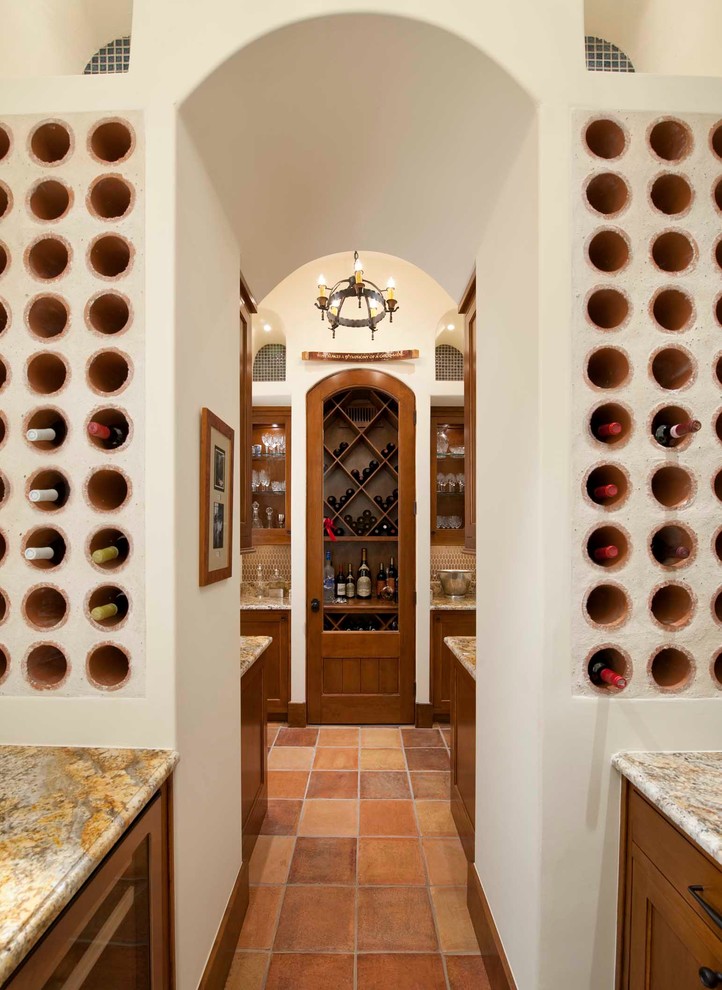 This is an example of a mediterranean wine cellar in Dallas with terra-cotta floors and storage racks.