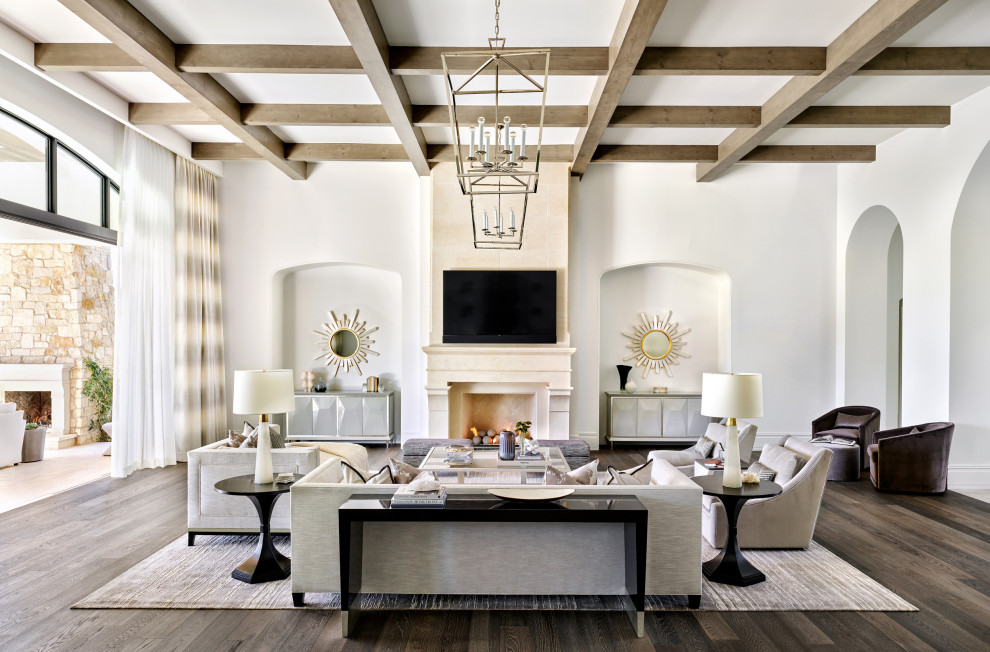 Photo of a mediterranean open concept family room in Phoenix with white walls, dark hardwood floors, a standard fireplace, a wall-mounted tv, brown floor and exposed beam.