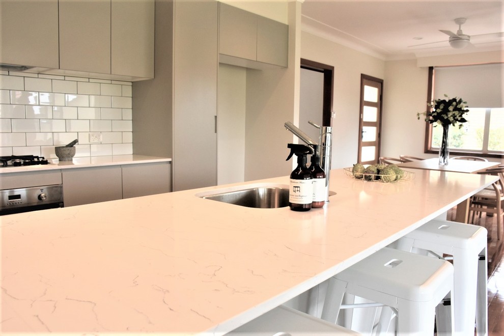 Inspiration for a mid-sized contemporary galley open plan kitchen in Newcastle - Maitland with an undermount sink, flat-panel cabinets, grey cabinets, quartz benchtops, white splashback, subway tile splashback, stainless steel appliances, medium hardwood floors, with island, brown floor and white benchtop.