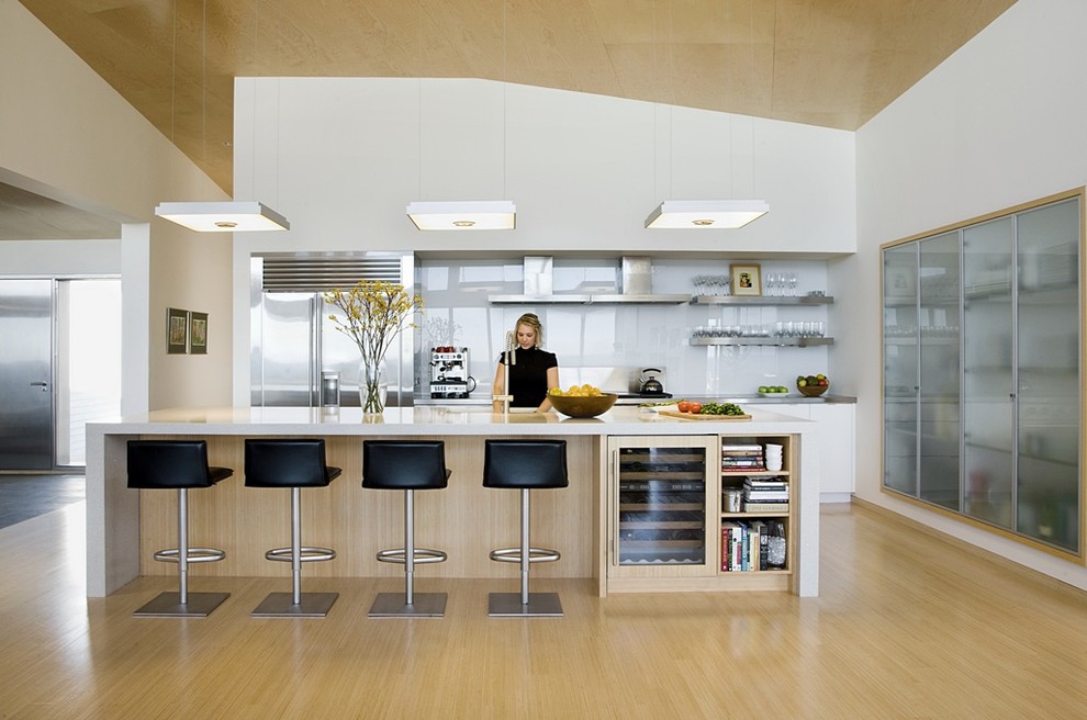 Photo of a large modern single-wall open plan kitchen in Boston with an undermount sink, flat-panel cabinets, white cabinets, concrete benchtops, stainless steel appliances, light hardwood floors, with island and beige floor.