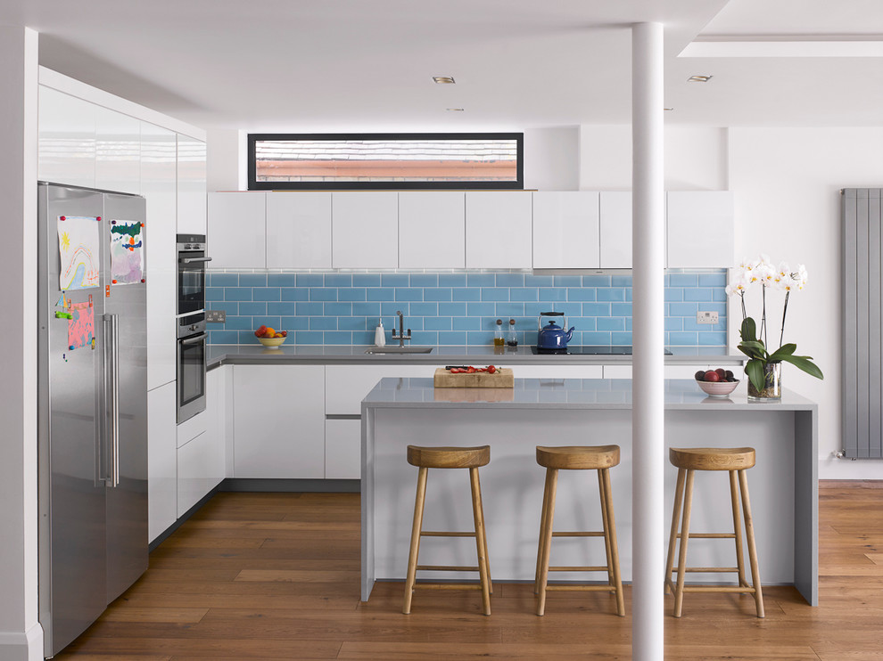 Inspiration for a contemporary l-shaped kitchen in London with an undermount sink, flat-panel cabinets, white cabinets, blue splashback, subway tile splashback, stainless steel appliances, medium hardwood floors and with island.