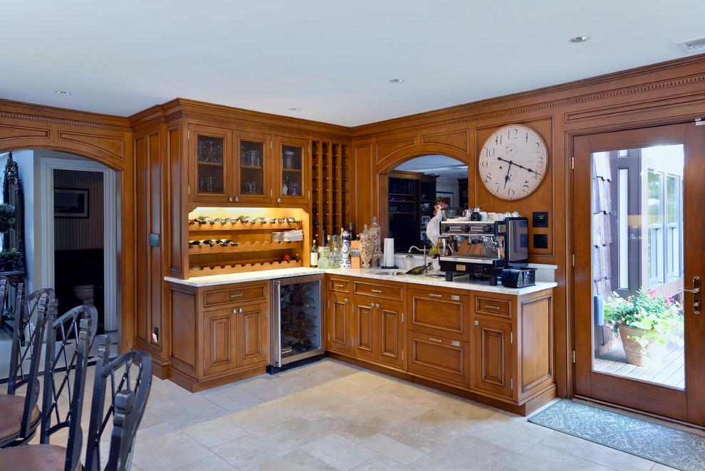 Photo of a mid-sized l-shaped wet bar in New York with an undermount sink, recessed-panel cabinets, medium wood cabinets, limestone benchtops and limestone floors.