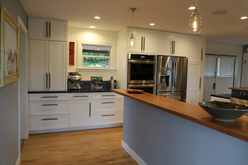 Mid-sized transitional u-shaped medium tone wood floor and brown floor eat-in kitchen photo with shaker cabinets, white cabinets, granite countertops, blue backsplash, stainless steel appliances, black countertops, an undermount sink, stone tile backsplash and a peninsula