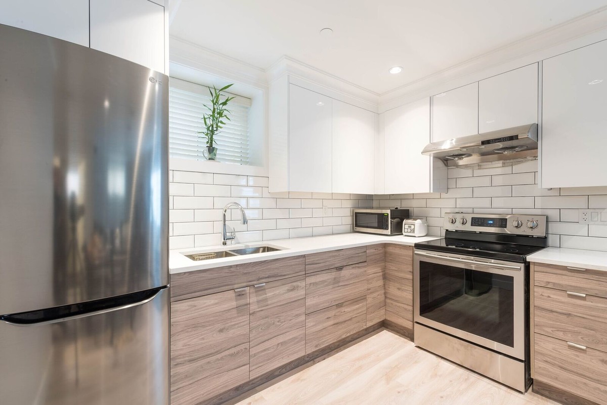 This is an example of a l-shaped separate kitchen in Vancouver with a drop-in sink, flat-panel cabinets, white cabinets, solid surface benchtops, white splashback, subway tile splashback, stainless steel appliances, plywood floors, no island and beige floor.