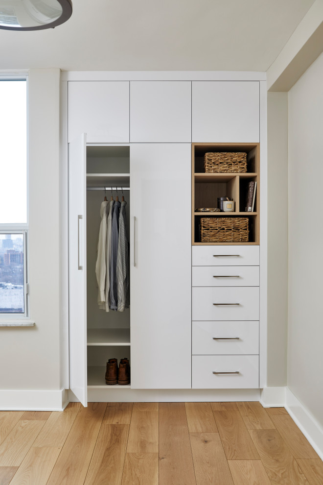Design ideas for a small contemporary gender-neutral storage and wardrobe in Toronto with flat-panel cabinets, white cabinets, light hardwood floors and brown floor.