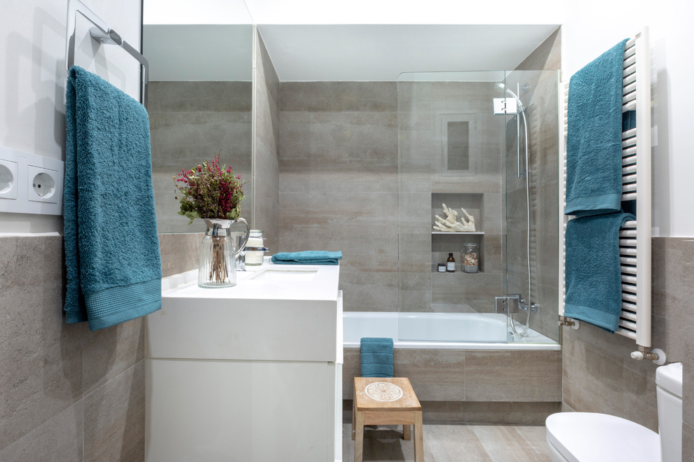 Photo of a small contemporary kids bathroom in Madrid with an alcove tub, a wall-mount toilet, gray tile, cement tile, white walls, cement tiles, an undermount sink, engineered quartz benchtops, grey floor, a sliding shower screen, white benchtops, furniture-like cabinets, white cabinets and a shower/bathtub combo.