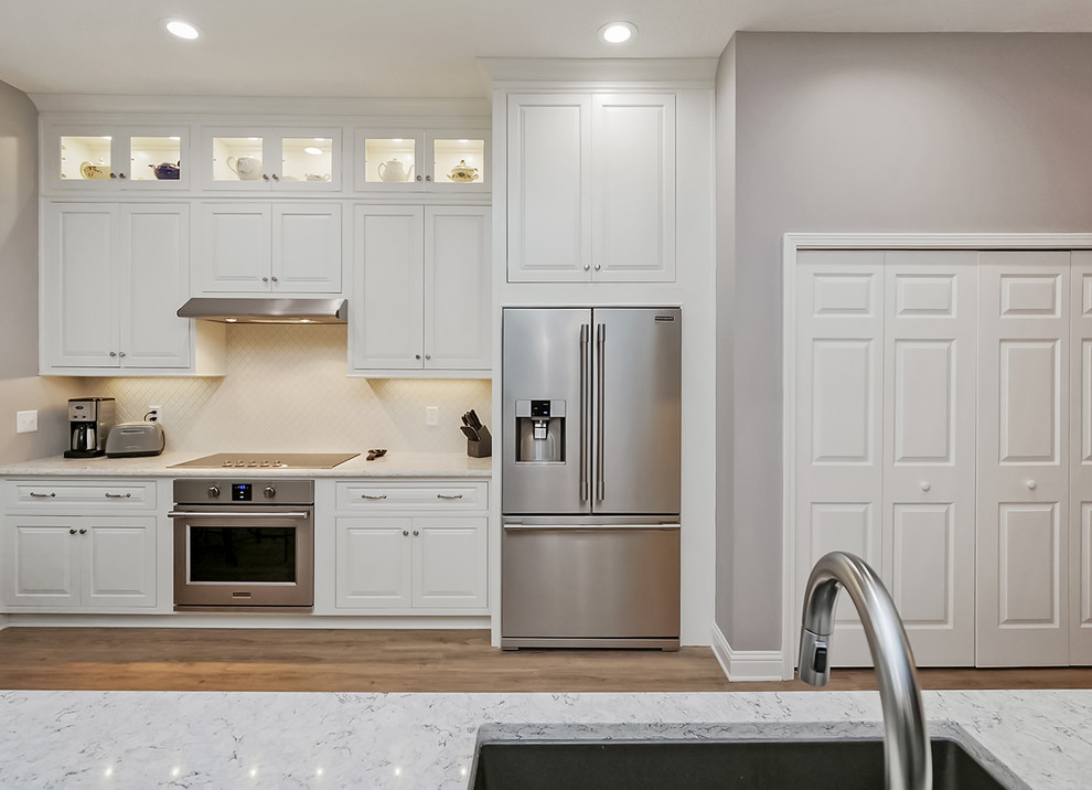 Design ideas for a mid-sized transitional galley open plan kitchen in Jacksonville with an undermount sink, beaded inset cabinets, white cabinets, quartz benchtops, white splashback, ceramic splashback, stainless steel appliances, vinyl floors, a peninsula, beige floor and grey benchtop.
