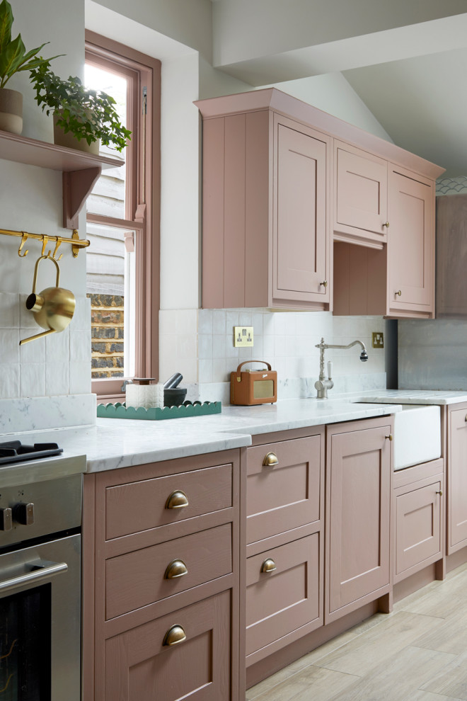 Design ideas for a mid-sized modern galley eat-in kitchen in London with a farmhouse sink, shaker cabinets, pink cabinets, marble benchtops, white splashback, ceramic splashback, stainless steel appliances, ceramic floors, no island and white benchtop.