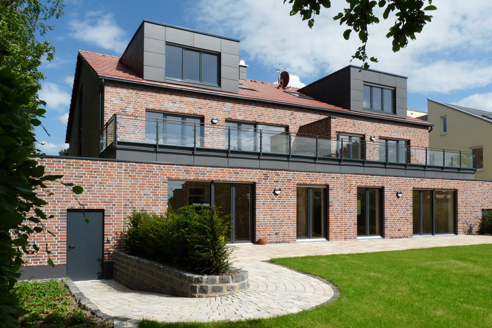 Mid-sized contemporary two-storey brick red apartment exterior in Dortmund with a gable roof and a tile roof.