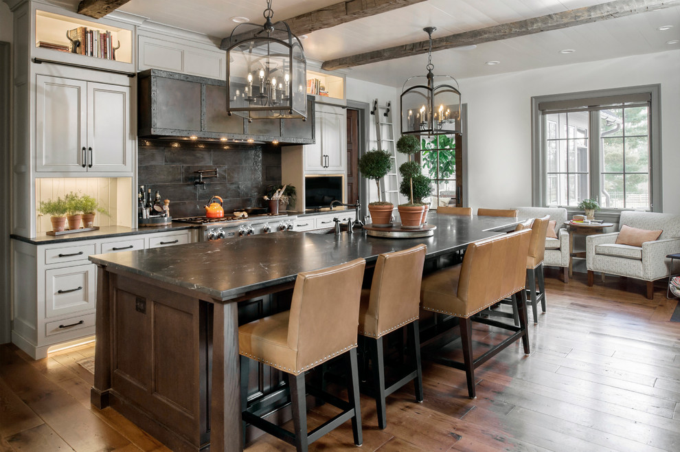 This is an example of a large traditional open plan kitchen in Columbus with a farmhouse sink, with island, brown floor, grey benchtop, brown splashback, stainless steel appliances, medium hardwood floors, beaded inset cabinets and white cabinets.
