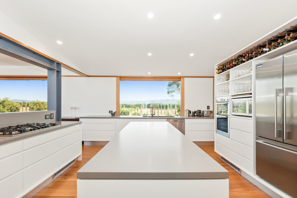 This is an example of a large modern u-shaped kitchen pantry in Central Coast with an undermount sink, white cabinets, quartz benchtops, grey splashback, stone slab splashback, stainless steel appliances, light hardwood floors, with island, brown floor and grey benchtop.