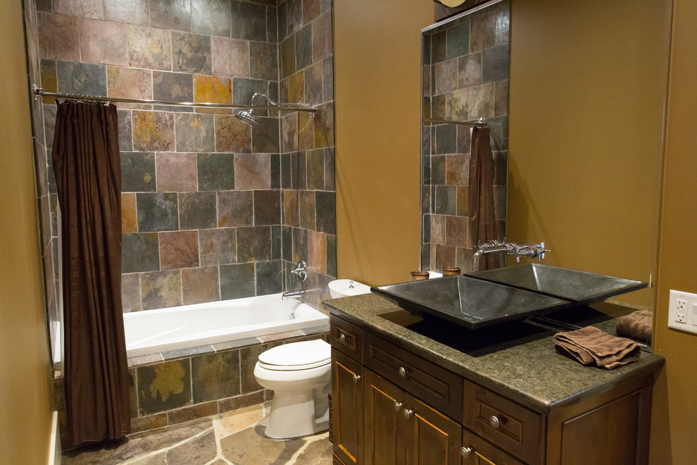 This is an example of a mid-sized country 3/4 bathroom in Toronto with recessed-panel cabinets, brown cabinets, a drop-in tub, a shower/bathtub combo, multi-coloured tile, slate, slate floors, a vessel sink, granite benchtops, brown floor, a shower curtain, a two-piece toilet and brown walls.