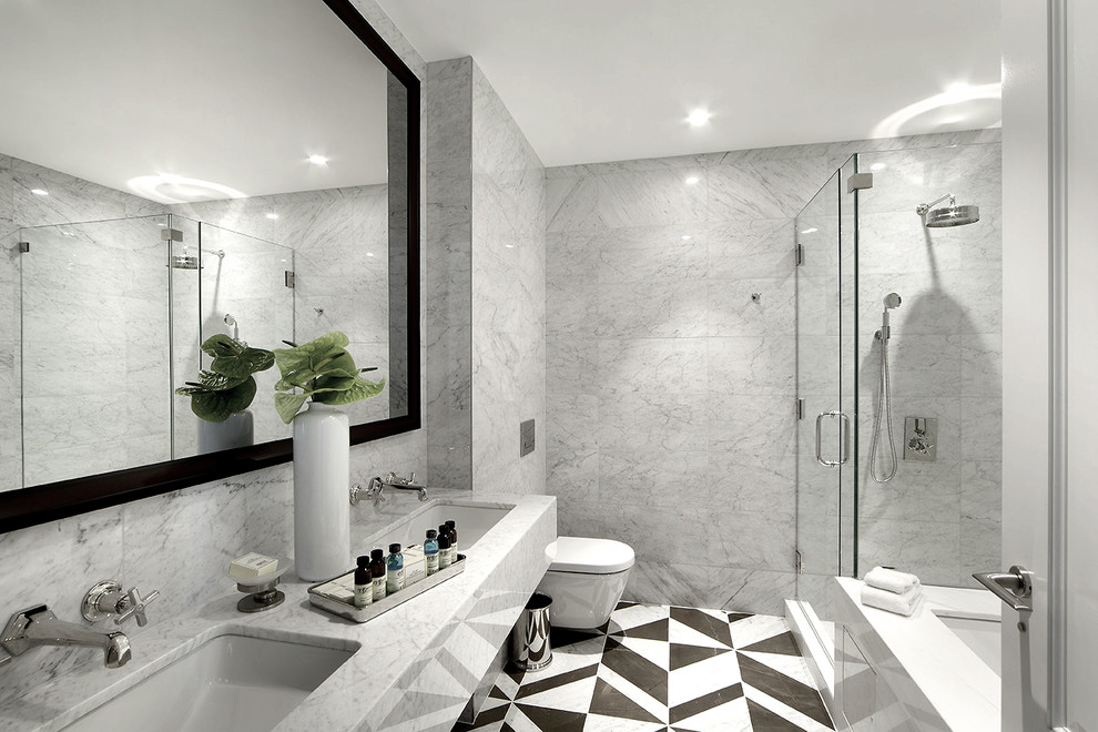 This is an example of a large contemporary master bathroom in New York with a drop-in tub, an alcove shower, a wall-mount toilet, gray tile, white tile, an undermount sink, marble benchtops, a hinged shower door and marble.