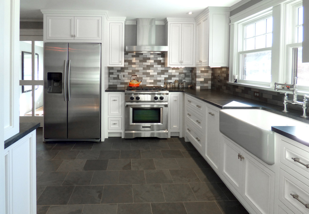Photo of a mid-sized transitional l-shaped eat-in kitchen in Boston with a farmhouse sink, raised-panel cabinets, white cabinets, granite benchtops, metallic splashback, metal splashback, stainless steel appliances, with island and slate floors.