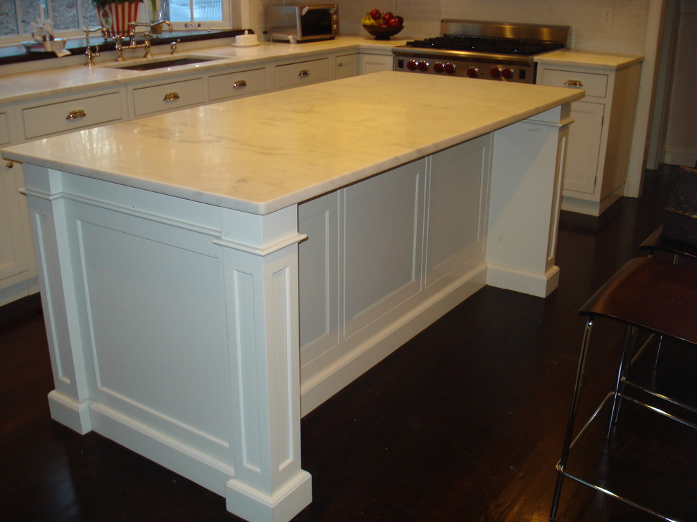 This is an example of a mid-sized traditional l-shaped kitchen in New York with an undermount sink, recessed-panel cabinets, white cabinets, marble benchtops, white splashback, panelled appliances, dark hardwood floors and with island.