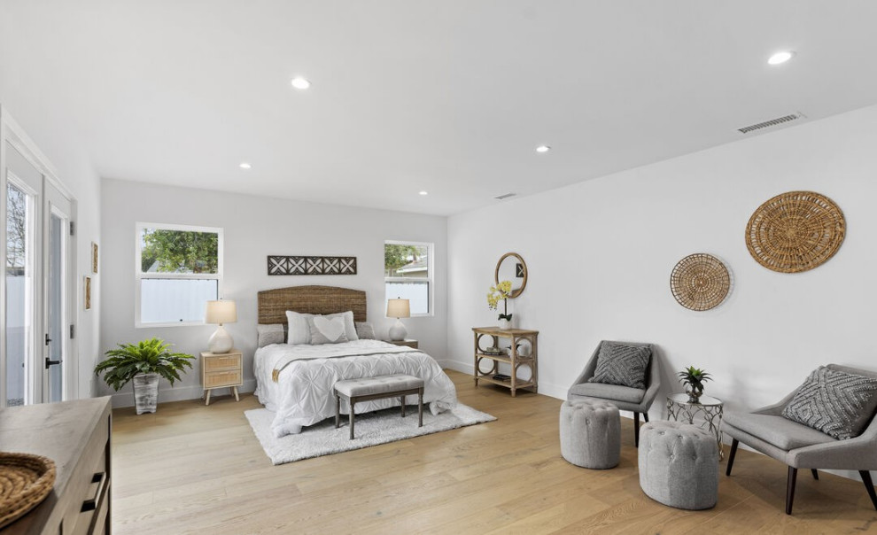 Cette photo montre une très grande chambre parentale tendance avec un mur blanc, parquet clair et un sol marron.
