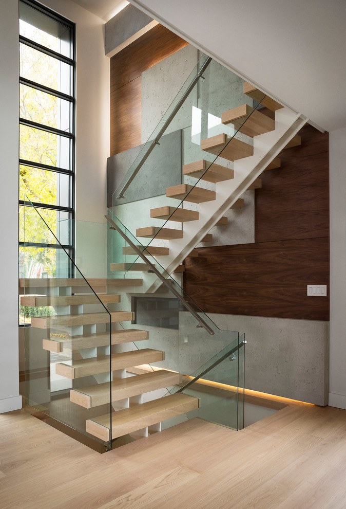 This is an example of a large contemporary wood u-shaped staircase in Toronto with open risers and glass railing.