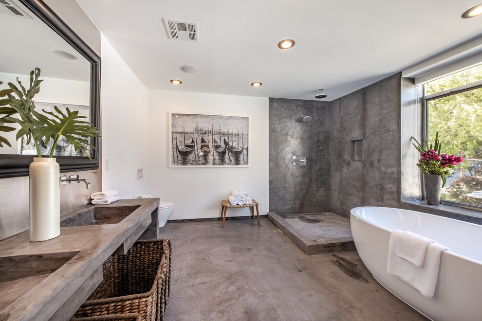 Large contemporary master bathroom in Los Angeles with a freestanding tub, gray tile, white walls, a trough sink, grey floor, grey benchtops, open cabinets, an open shower, a wall-mount toilet, cement tile, concrete floors, concrete benchtops and an open shower.
