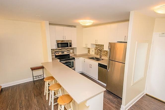 Example of a mid-sized transitional single-wall medium tone wood floor and brown floor open concept kitchen design in Chicago with white cabinets, multicolored backsplash, stainless steel appliances, a peninsula, a drop-in sink, flat-panel cabinets, granite countertops and glass tile backsplash