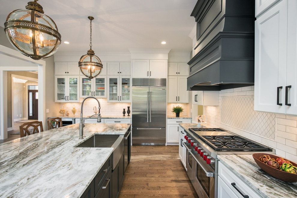 Inspiration for a traditional kitchen in Grand Rapids with a farmhouse sink, recessed-panel cabinets, white cabinets, granite benchtops, white splashback, subway tile splashback, stainless steel appliances, dark hardwood floors, with island and brown floor.