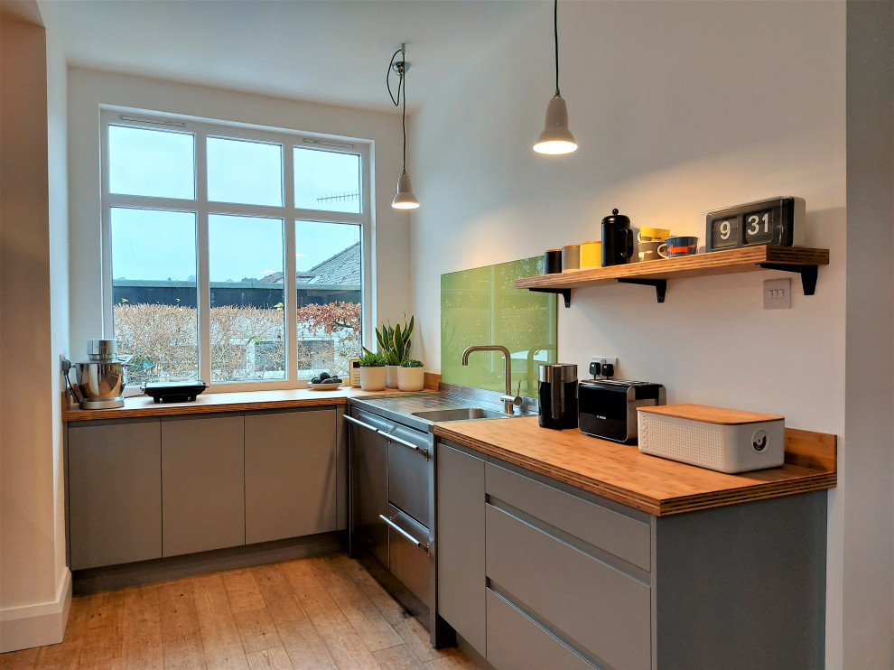 Idéer för att renovera ett litet funkis brun brunt kök, med släta luckor, grå skåp, träbänkskiva, grönt stänkskydd, glaspanel som stänkskydd, rostfria vitvaror och brunt golv
