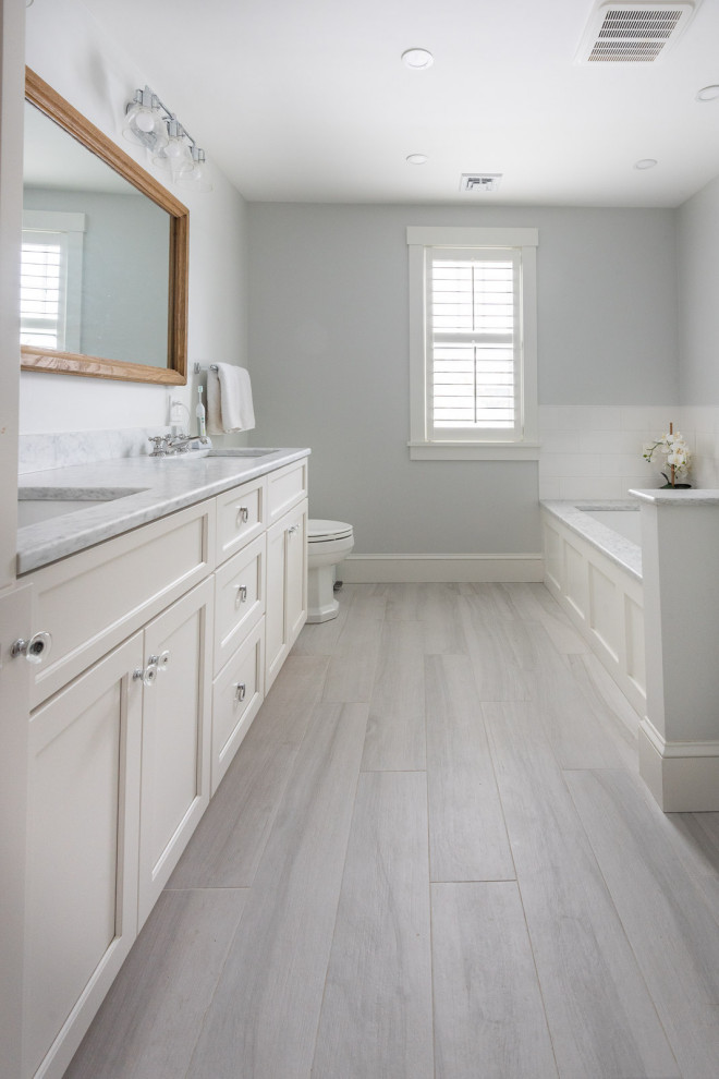Photo of a large transitional master bathroom in Boston with shaker cabinets, white cabinets, an undermount tub, an alcove shower, a one-piece toilet, white tile, ceramic tile, grey walls, porcelain floors, an undermount sink, engineered quartz benchtops, grey floor, a hinged shower door, white benchtops, a double vanity and a built-in vanity.