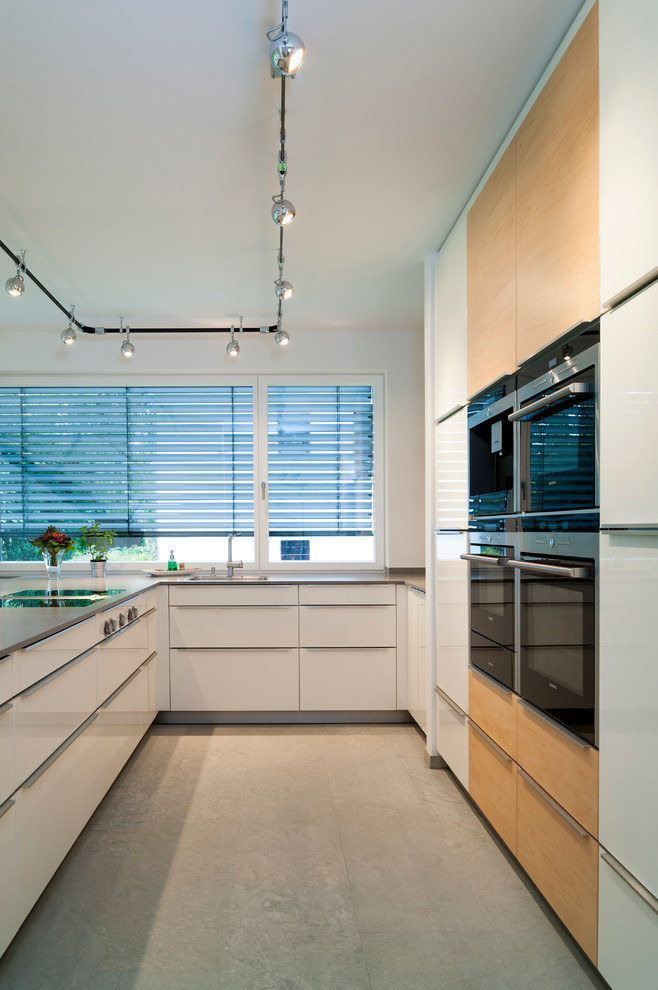 This is an example of a mid-sized contemporary u-shaped open plan kitchen in Hanover with flat-panel cabinets, white cabinets, white splashback, black appliances and with island.